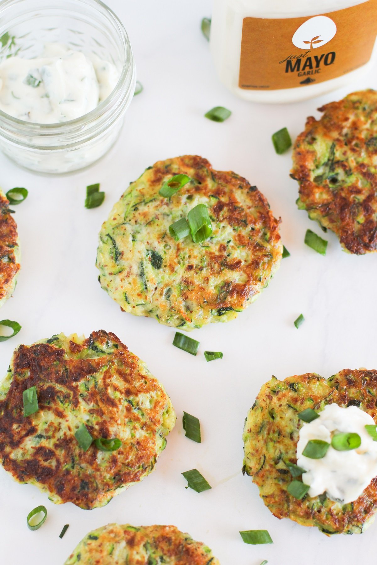 Gluten Free Zucchini Fritters with Herb-Garlic Aioli sitting on a white background, ready to eat