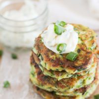 Stack of gluten-free zucchini fritters on a cutting board with aioli on top and sprinkled with green onions.