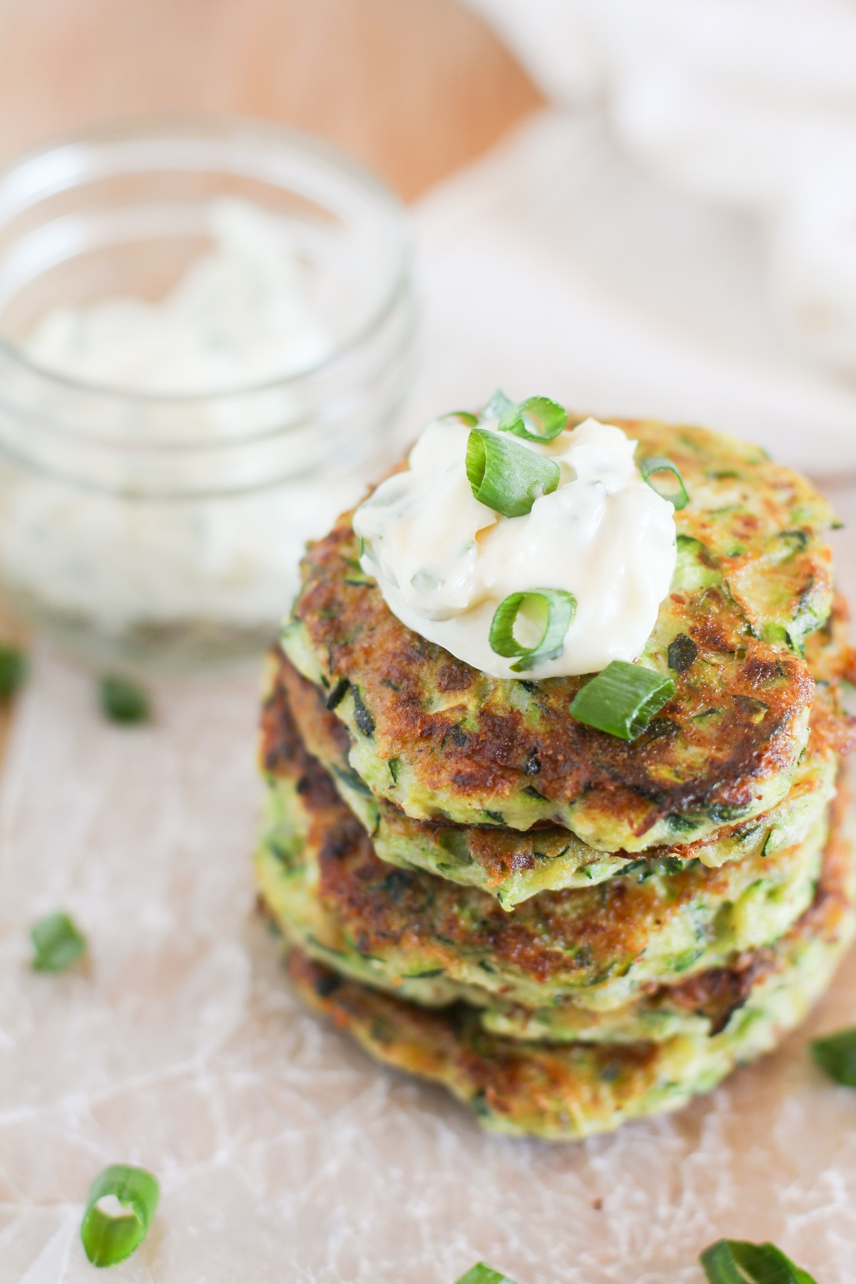 Stack of gluten-free zucchini fritters on a cutting board with aioli on top and sprinkled with green onions.