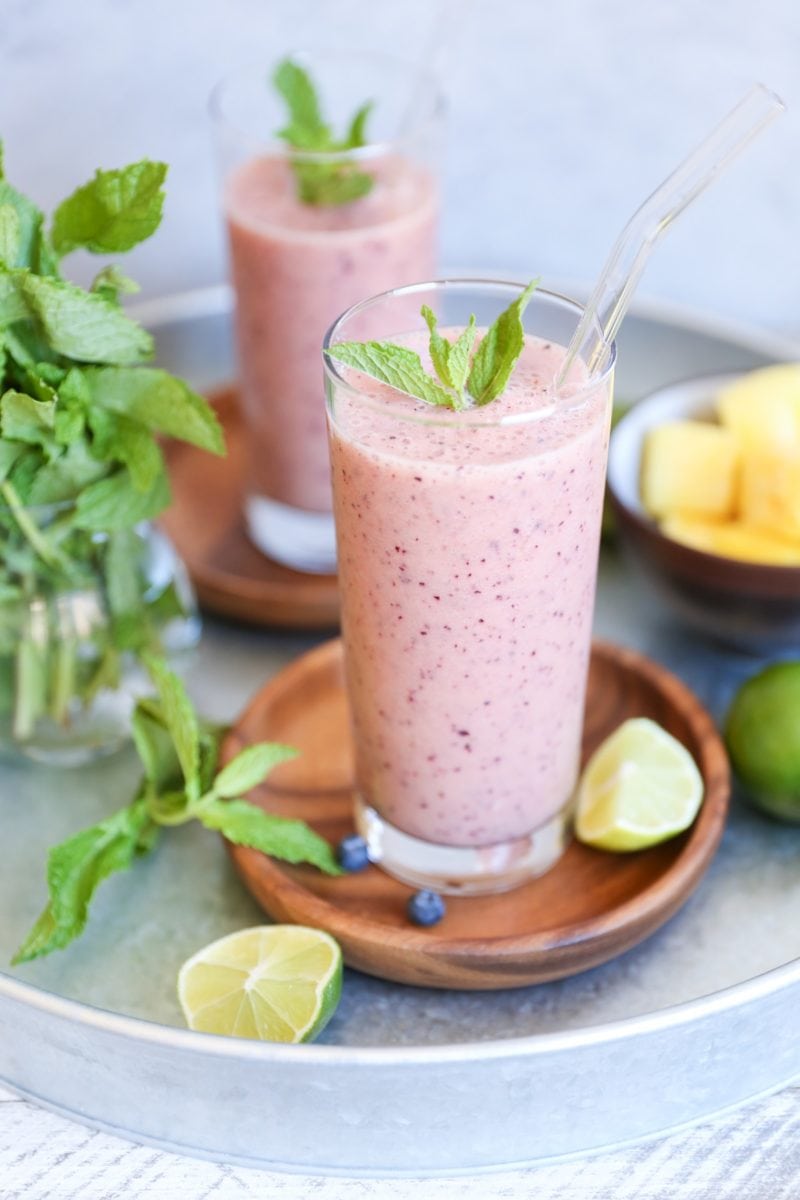 Two fruit smoothies in glasses in a serving tray with fresh fruit