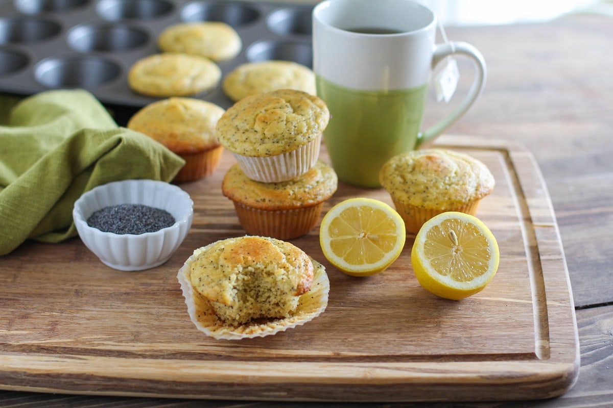 grain-free lemon poppy seed muffins fresh out of the oven sitting on a cutting board with a mug of tea and fresh lemons to the side.