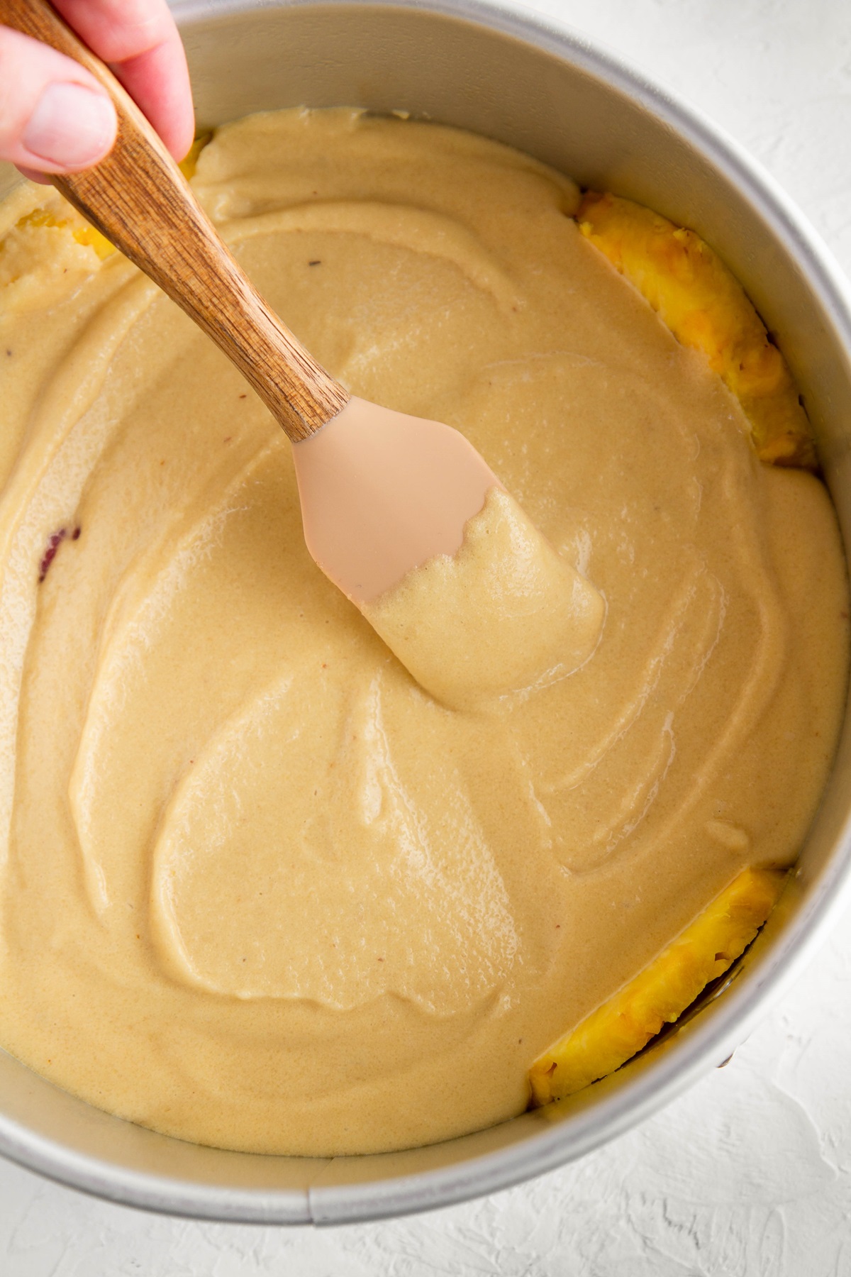 Cake batter being spread in a cake pan with a rubber spatula to make pineapple upside down cake.