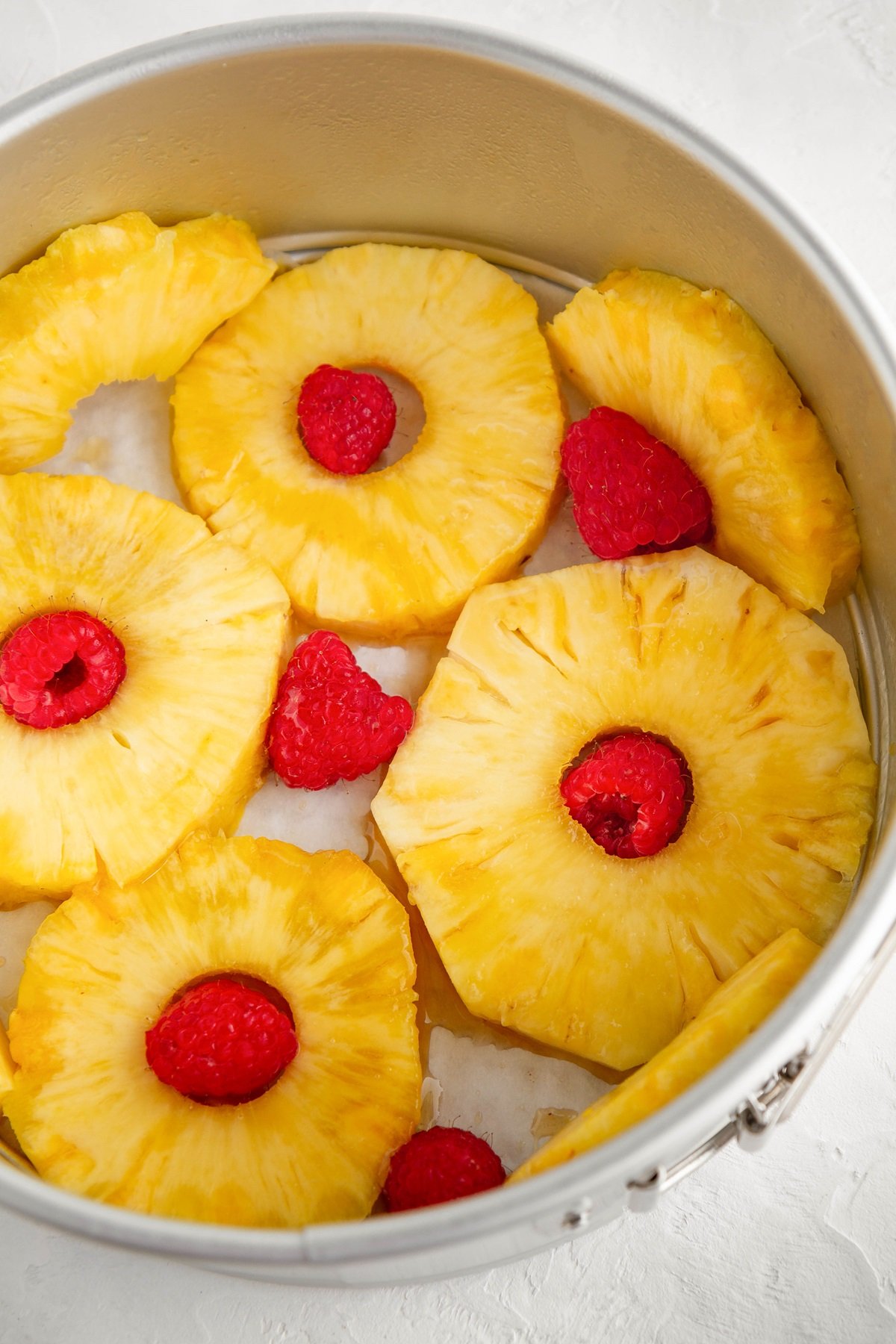 Fresh pineapple slices in the bottom of a cake pan with fresh raspberries to make pineapple cake.