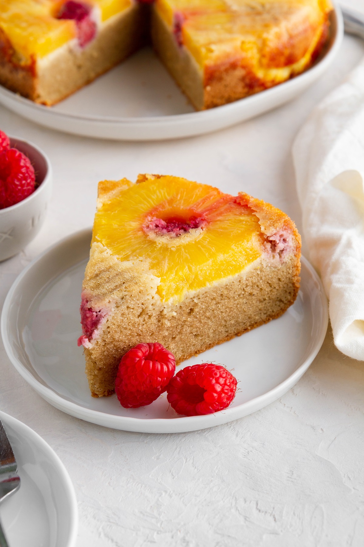 Slices of almond flour pineapple upside down cake on white plates with the full cake in the background.