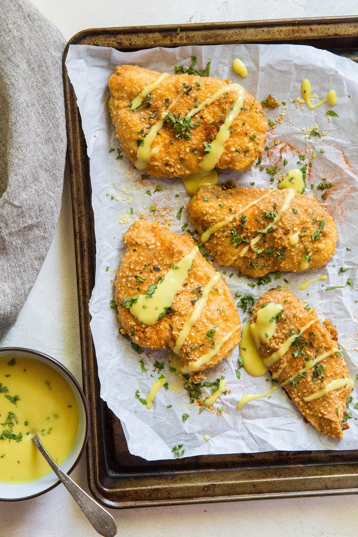 Baking sheet with pretzel crusted chicken on top with honey mustard sauce to the side. Chicken is drizzled with sauce and sprinkled with fresh parsley.