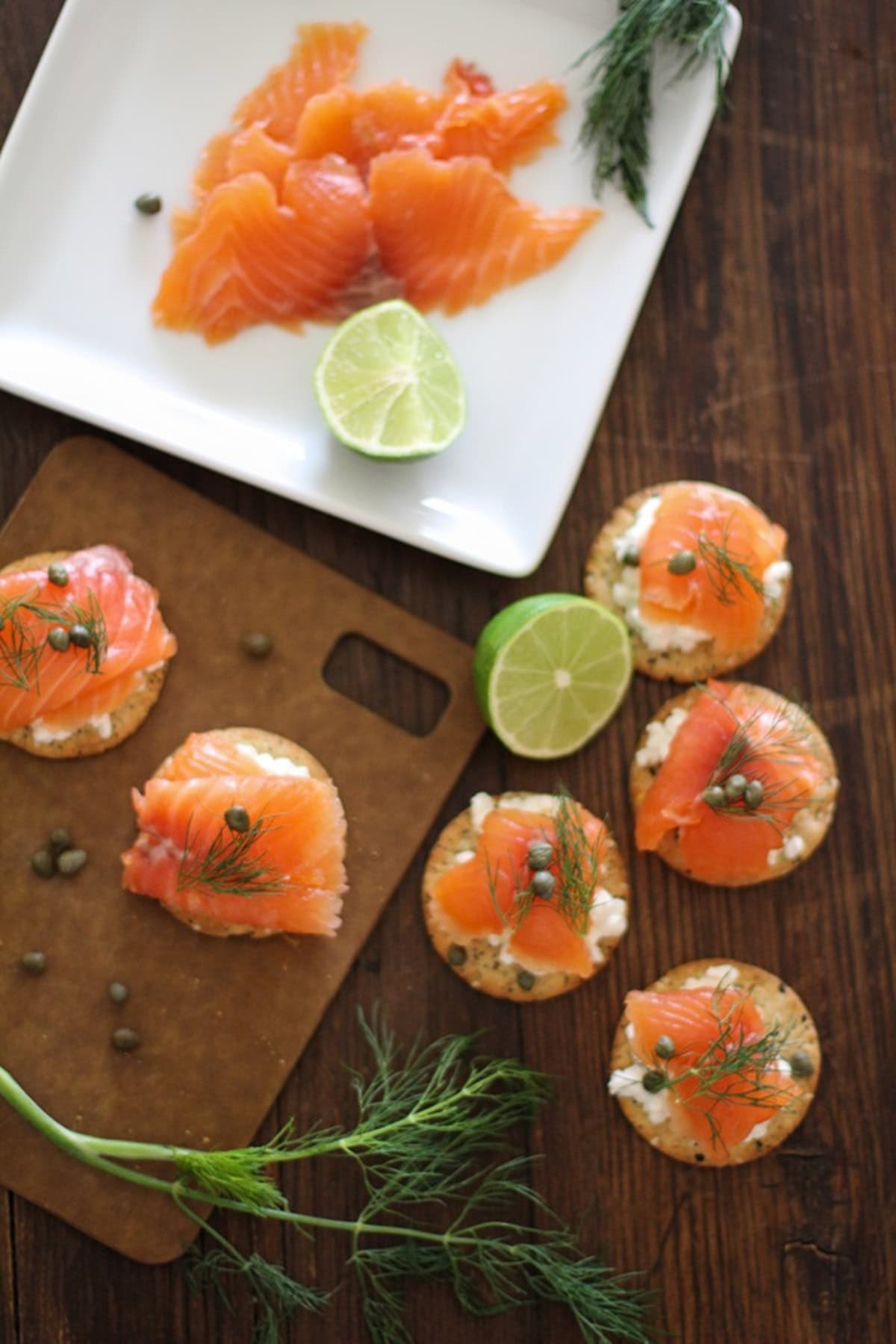 Swedish Gravlax (cured salmon) on crackers on a cutting board with fresh dill to the side.