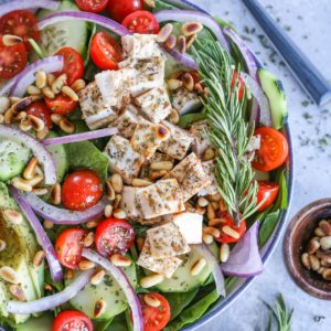Herby Greek Spinach Salad in a large bowl with a sliced open avocado, dried herbs, and a napkin to the side.