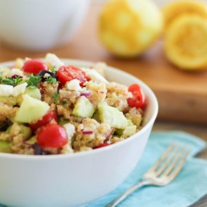 Greek Quinoa Salad recipe in a bowl on top of a blue napkin with a serving spoon to the side.