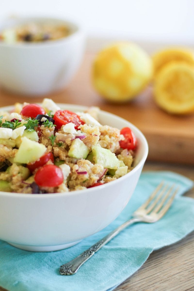 Greek Quinoa Salad recipe in a bowl on top of a blue napkin with a serving spoon to the side.