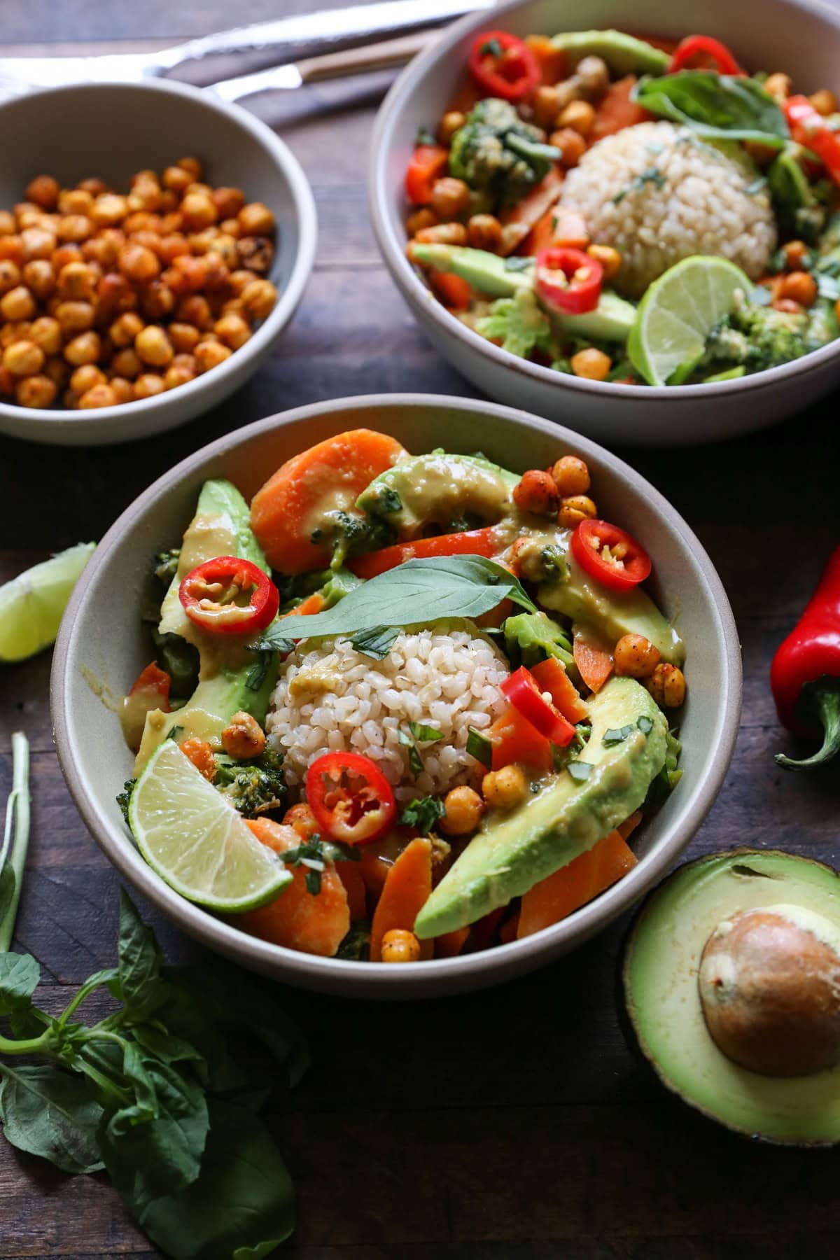 Two ceramic bowls full of avocado curry on a wooden table with fresh basil and lime.