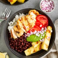 Grilled Cuban Mojo Chicken Bowls with fried plantains and mojo sauce in black bowls and a napkin to the side, ready to eat