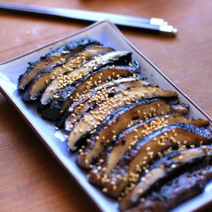 Grilled portobello mushroom cut into slices on a long blue plate with chopsticks and fresh ginger in the background, ready to serve as an appetizer.