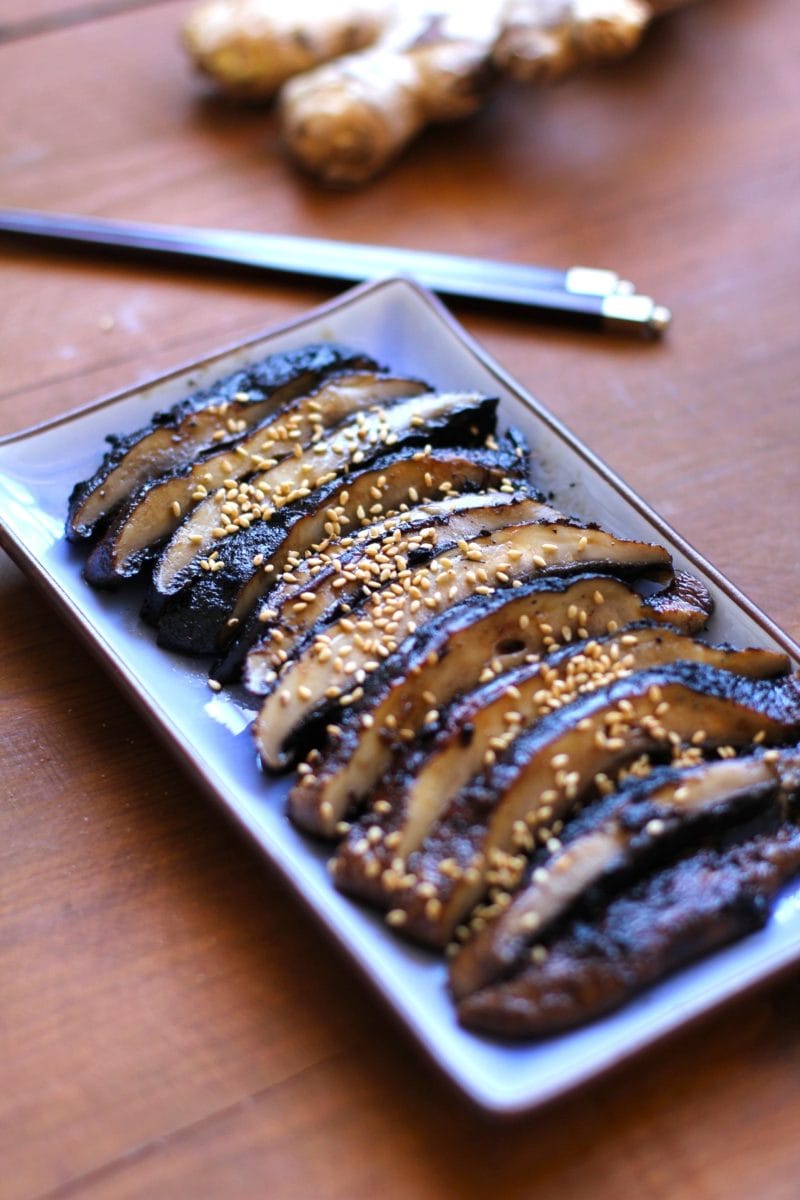 Grilled portobello mushroom cut into slices on a long blue plate with chopsticks and fresh ginger in the background, ready to serve as an appetizer.