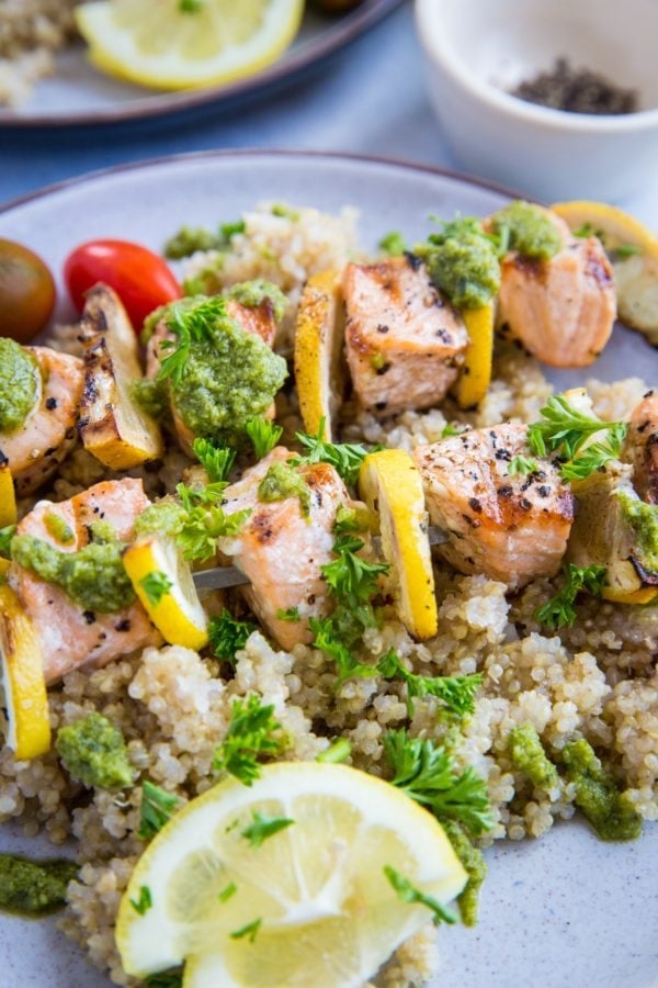 Grilled Salmon Kabobs close up with pesto sauce drizzled on top and fresh parsley sprinkled. Skewers on top of quinoa for serving.