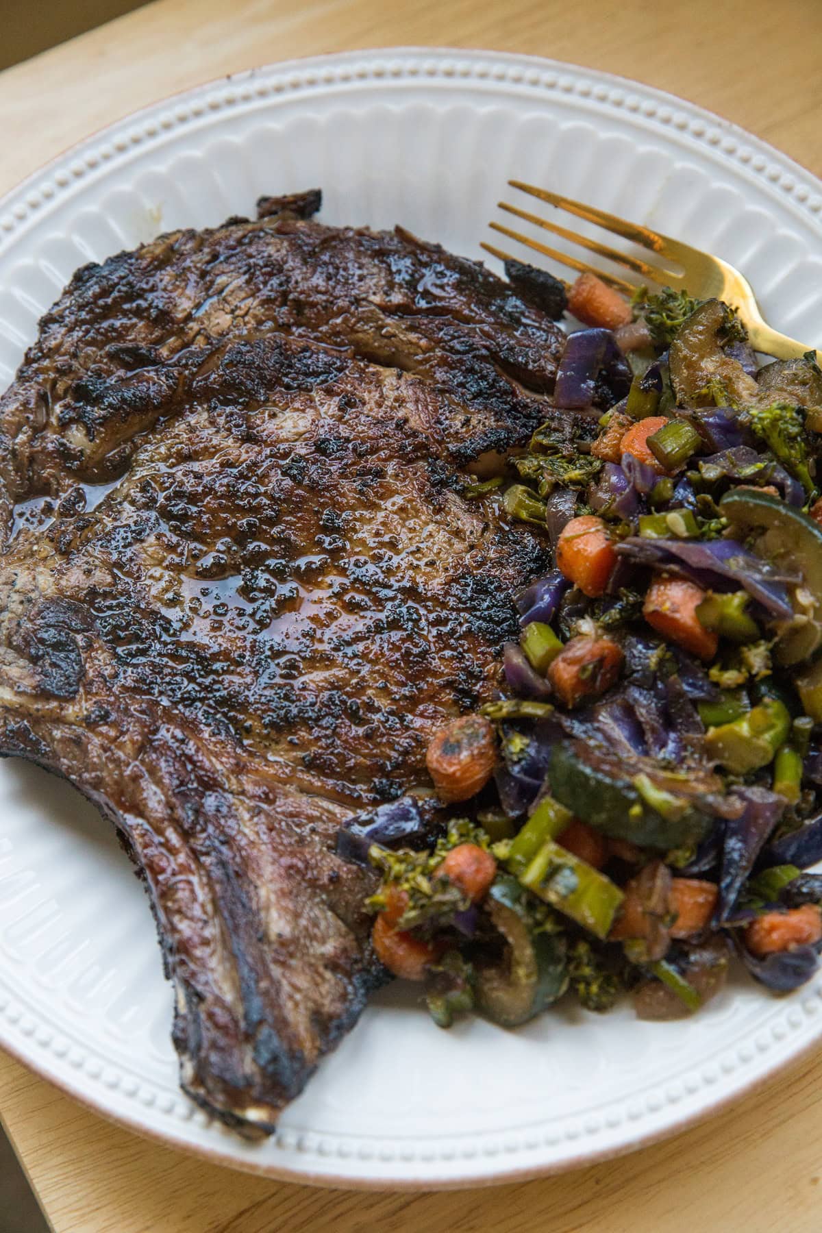 Grilled steak on a plate next to roasted vegetables, ready to ear.