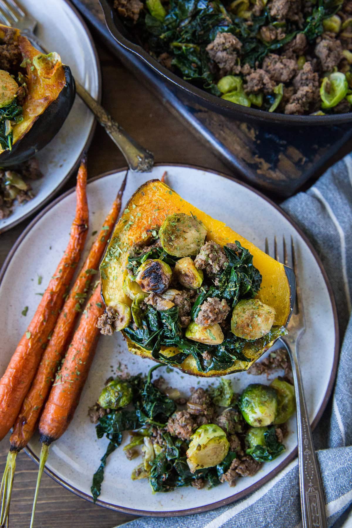Acorn squash stuffed with ground beef, kale, and brussels sprouts on a plate with roasted carrots to the side.