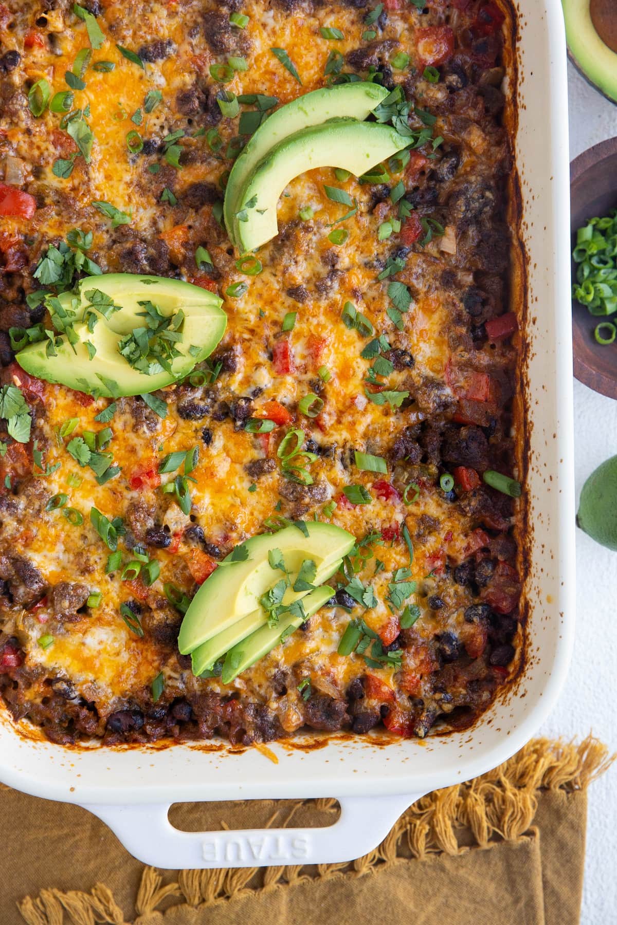 Ground Beef Taco Casserole in a white casserole dish with green onion and avocado on top.