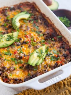 Casserole dish with ground beef casserole inside. Fresh avocado and a bowl of green onions to the side.