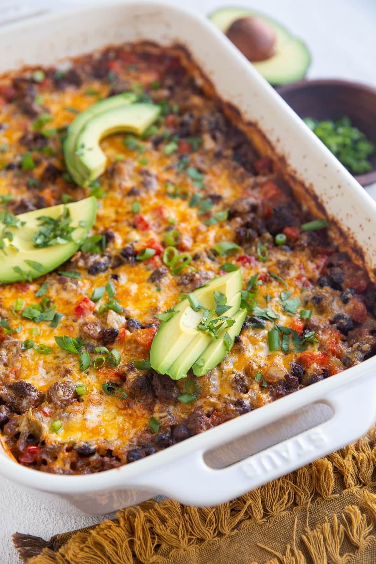 Casserole dish with ground beef casserole inside. Fresh avocado and a bowl of green onions to the side.