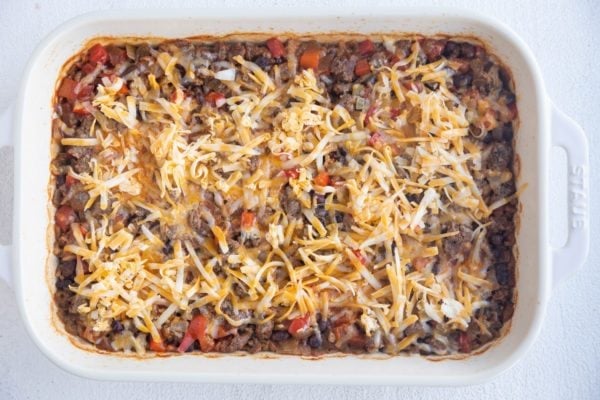 Partially baked casserole with cheese on top.