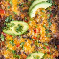 Close up of a ground beef taco casserole with sliced avocado and cilantro on top.