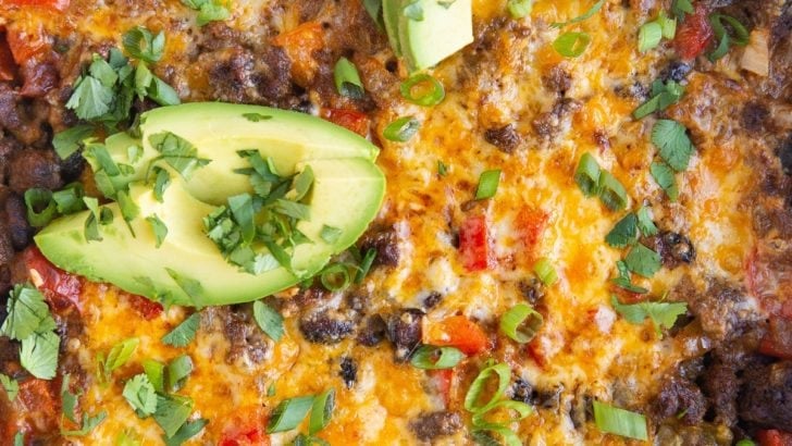 Close up of a ground beef taco casserole with sliced avocado and cilantro on top.