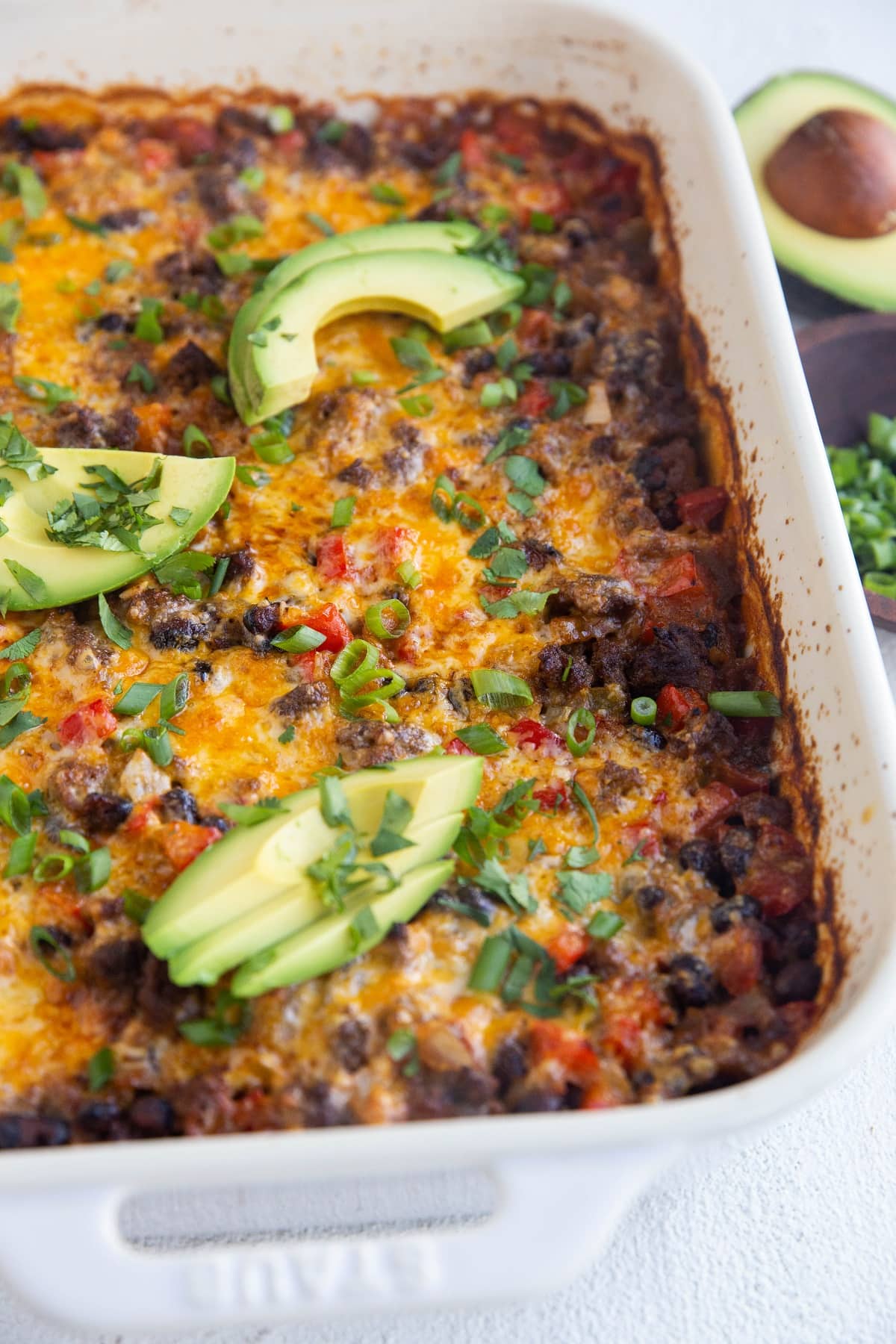 Full casserole dish of ground beef taco casserole with avocado on top, ready to serve.