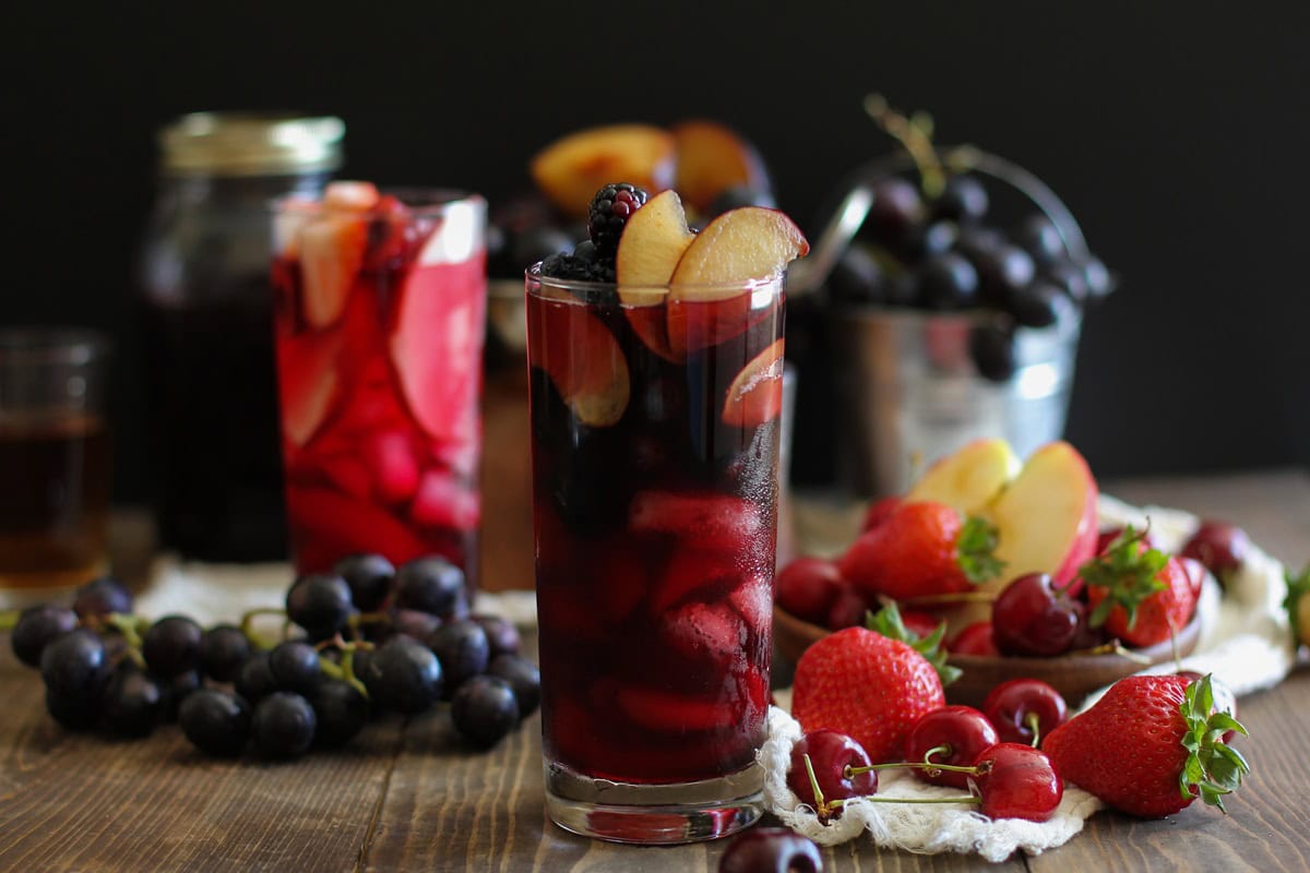 Two glasses of sangria with fresh fruit all around. One glass is dark to emulate witch's brew and the other is bright blood red.