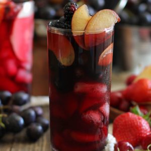 Two tall glasses of Halloween sangria. One is black to mimic witch's brew and the other is bright blood red to mimic blood. Both are packed with fresh fruit that is dark and spooky,