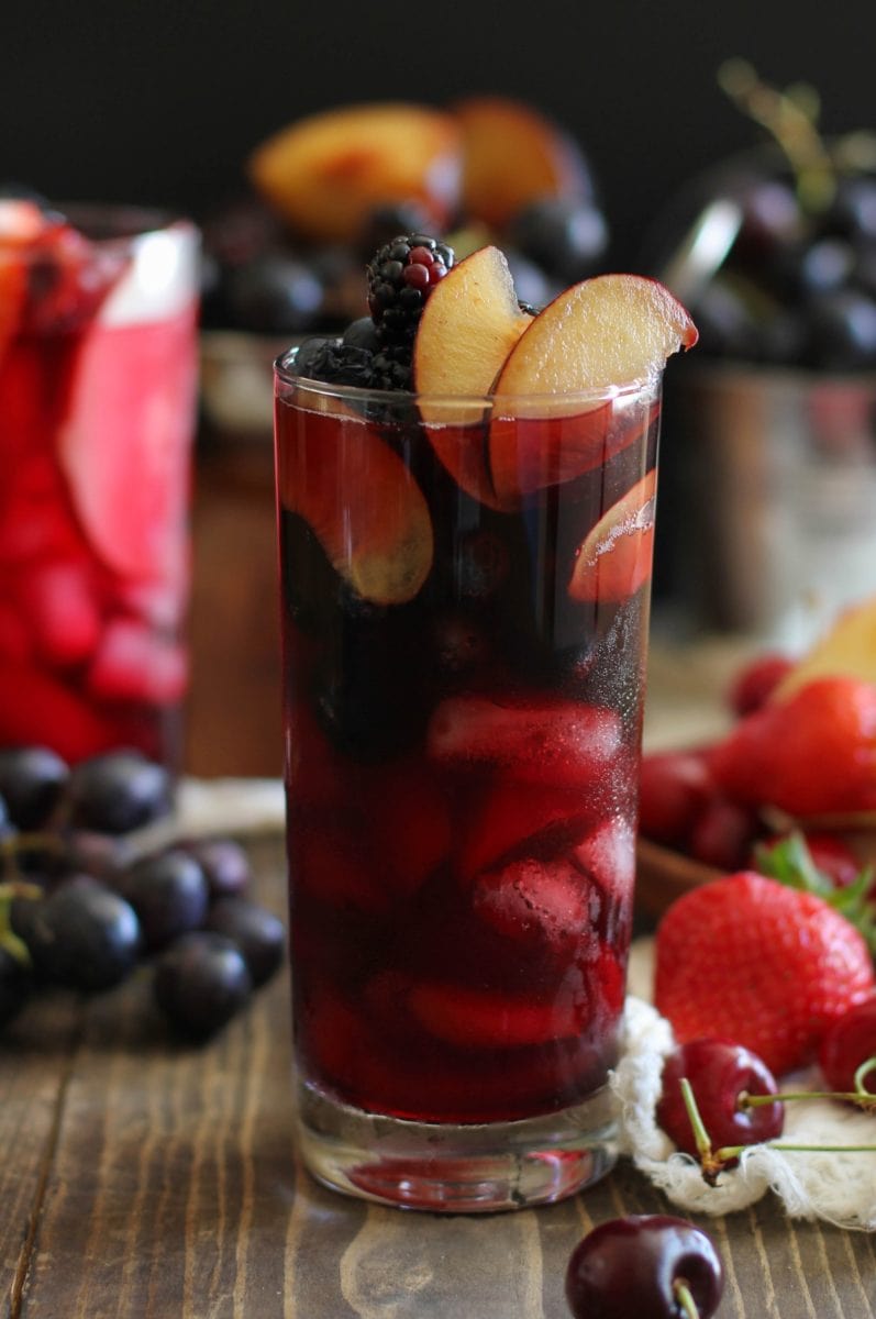 Two tall glasses of Halloween sangria. One is black to mimic witch's brew and the other is bright blood red to mimic blood. Both are packed with fresh fruit that is dark and spooky,