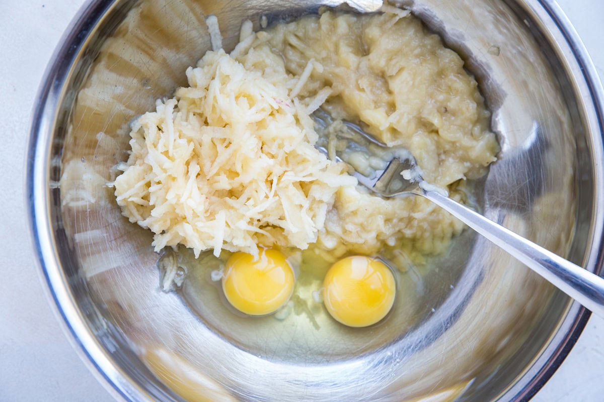 Stainless steel bowl with mashed banana, grated apples, and eggs.