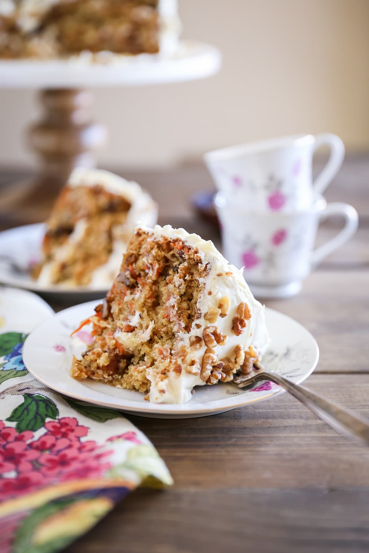 Two slices of healthy carrot cake made with almond flour on plates with cups of tea.
