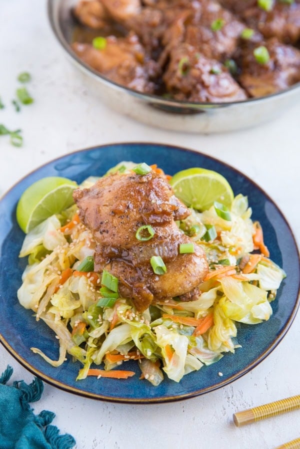 Filipino Chicken Adobo on top of sauteed cabbage on a blue plate with fresh limes to the side.