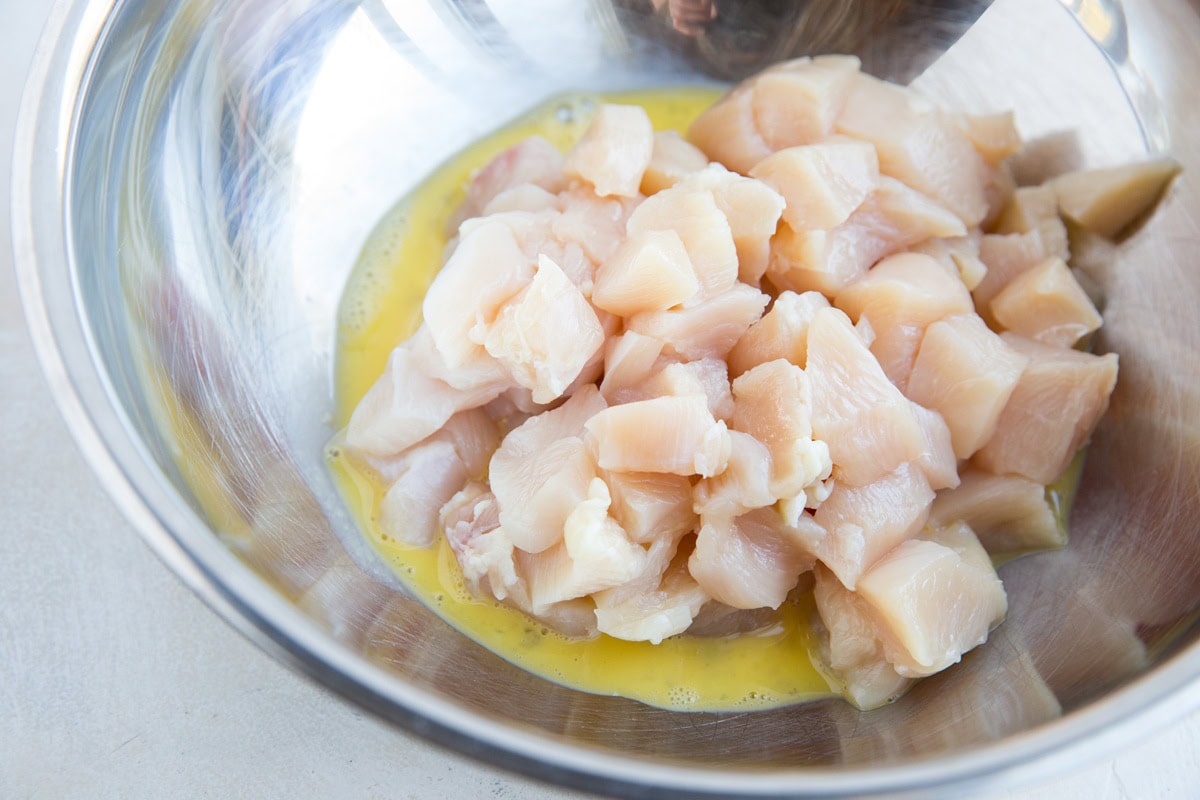 Chicken in a large stainless steel bowl sitting in an egg wash for healthy general chicken