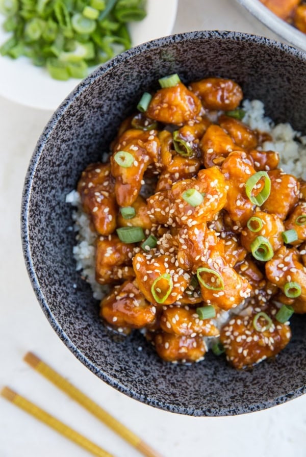 Large bowl full of rice and saucy general chicken sprinkled with sesame seeds and green onions. Ready to enjoy.