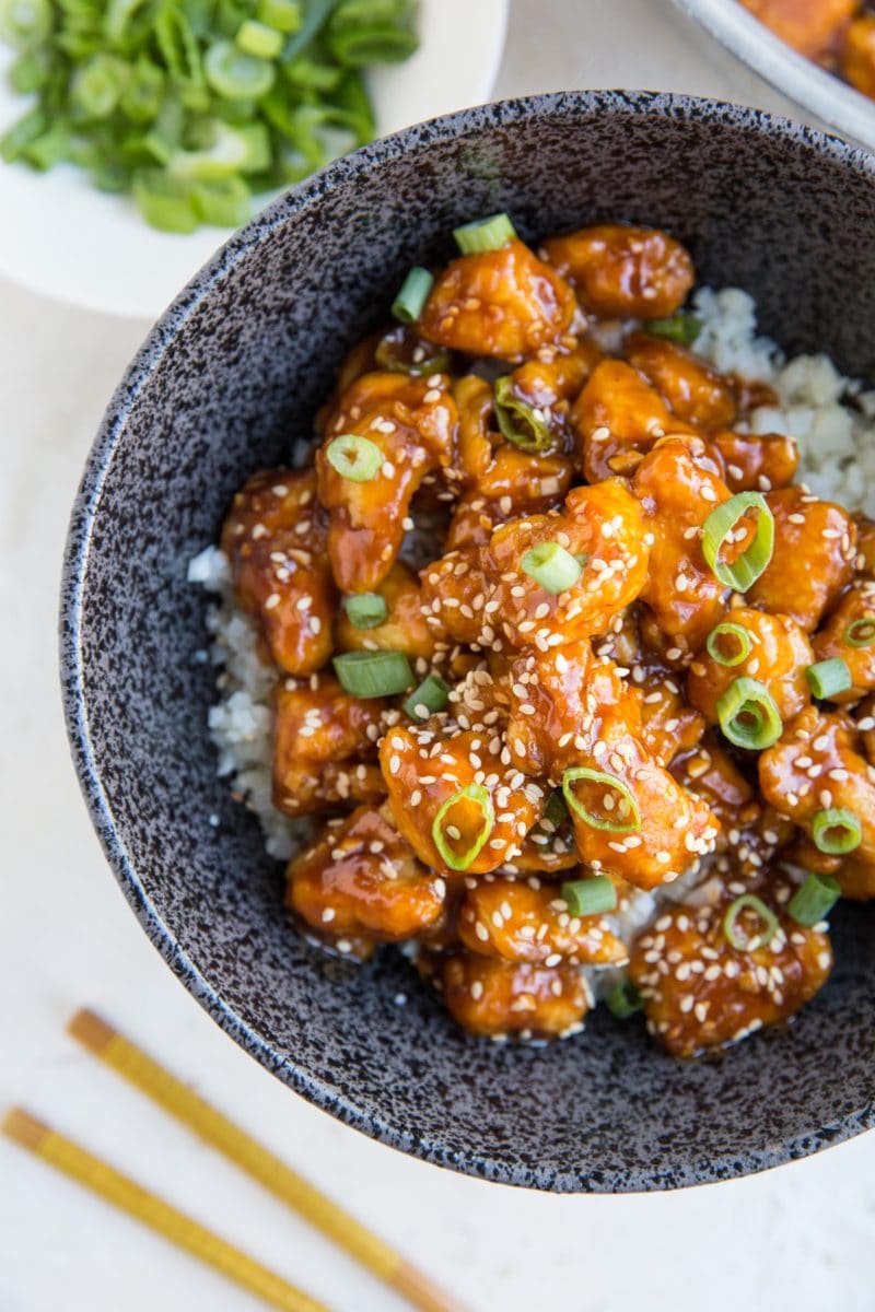 Large bowl full of rice and saucy general chicken sprinkled with sesame seeds and green onions. Ready to enjoy.