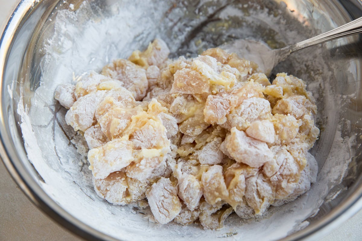 Stainless steel bowl full of chopped chicken breasts tossed in egg and flour to make breading.