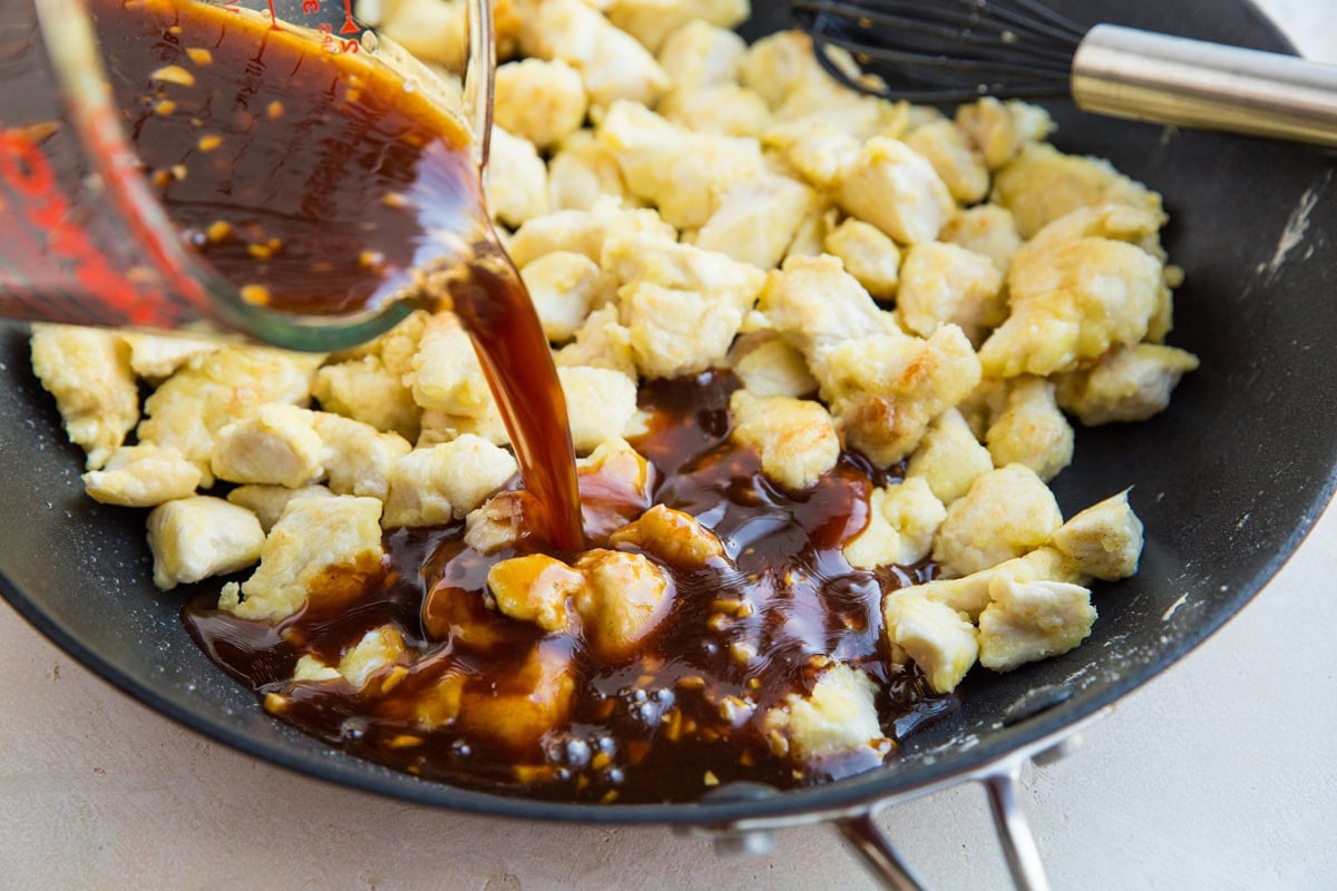 Pouring sweet and sour general chicken sauce into skillet with pan-fried chicken.