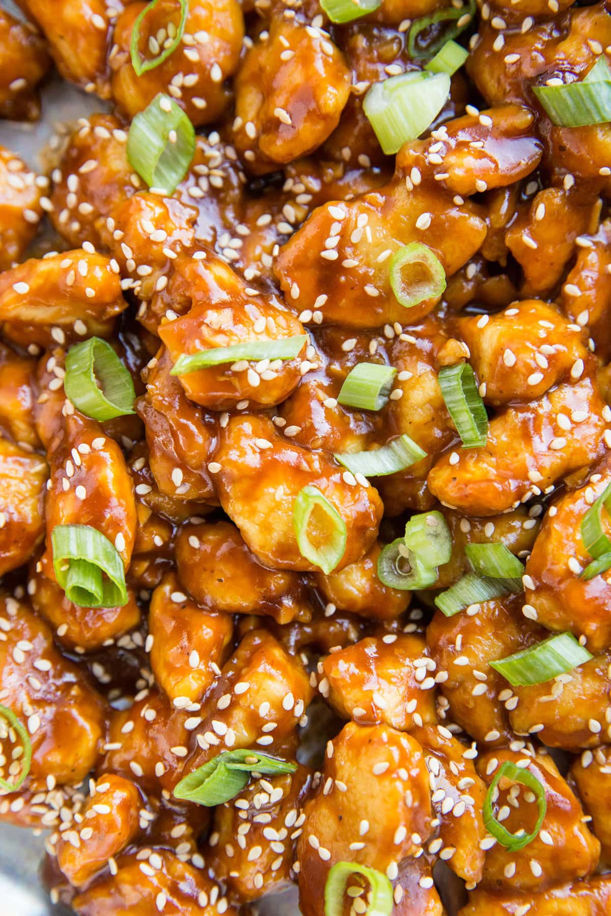 Large stainless steel skillet full of cooked general chicken sprinkled with green onions and sesame seeds.