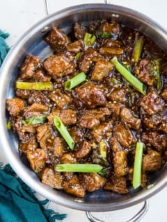 Stainless steel skillet full of healthy Mongolian beef with green onions on top and a blue napkin to the side.