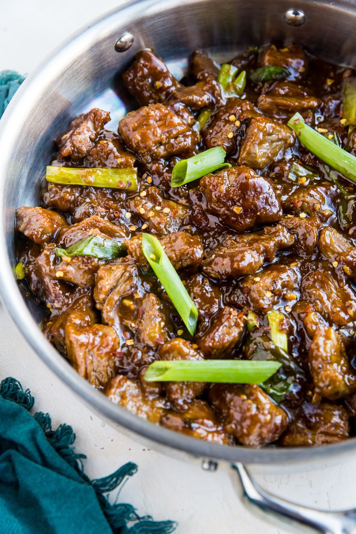 Stainless steel skillet full of healthy Mongolian beef with a blue napkin to the side. Ready to serve.