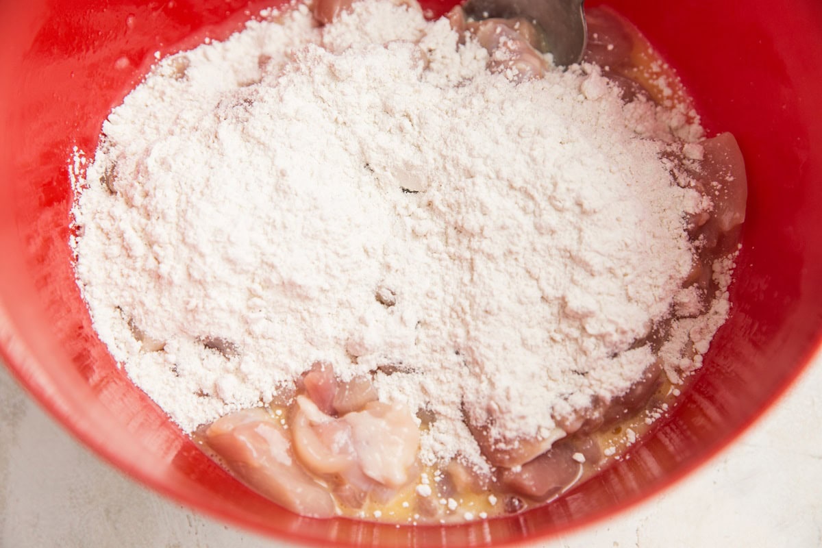 Chicken pieces coated in beaten egg with flour sprinkled on top to be mixed in.