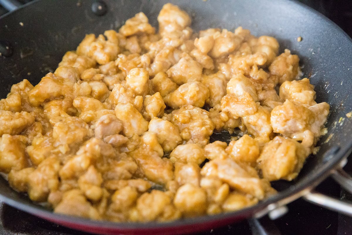 Orange chicken cooking in a skillet, almost finished.