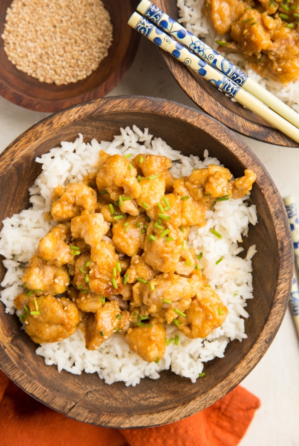 large wooden bowl full of rice and orange chicken with chop sticks and a red napkin.