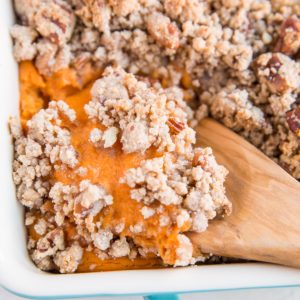 Blue casserole dish full of Sweet Potato Casserole with a wooden spoon scooping out some of the casserole.