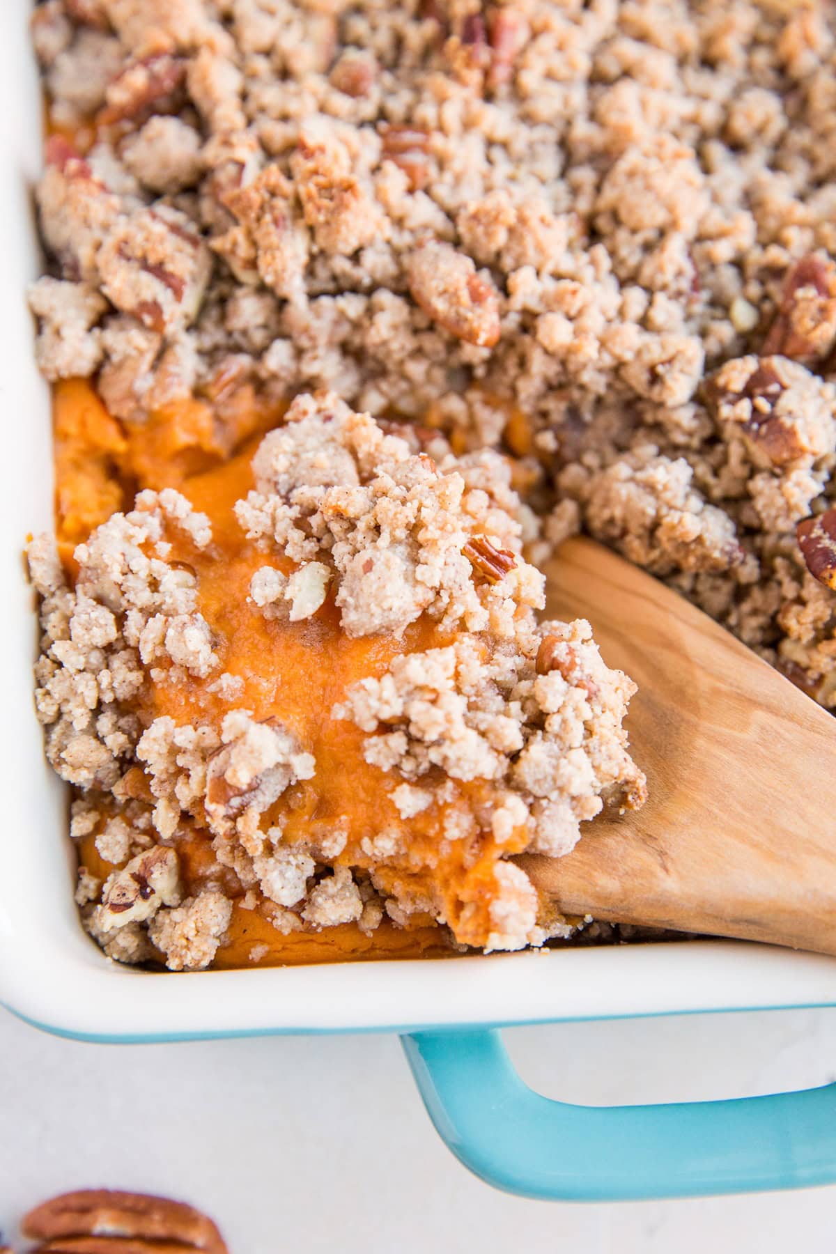 Blue casserole dish full of Sweet Potato Casserole with a wooden spoon scooping out some of the casserole.