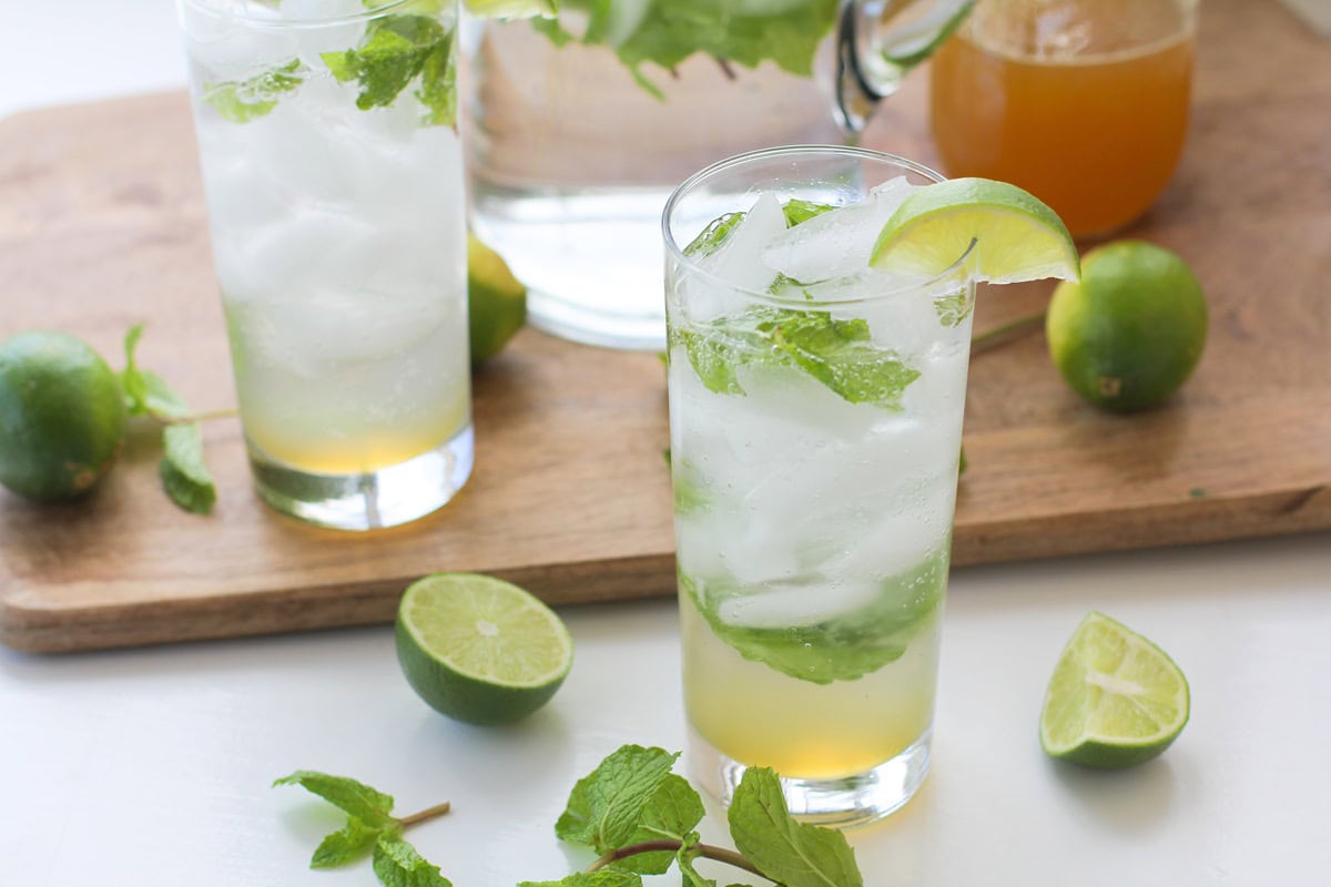 Two glasses of mint mojitos with fresh mint leaves and fresh limes all around.
