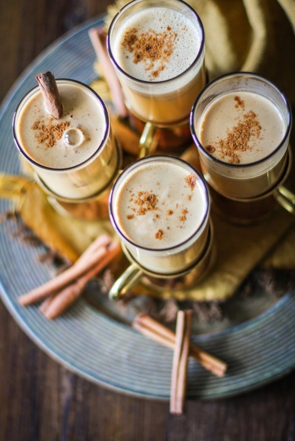 Four glasses of Hot Buttered Rum on a serving platter with cinnamon sticks around.