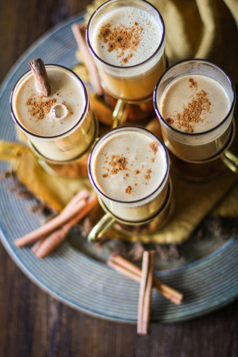 Four glasses of Hot Buttered Rum on a serving platter with cinnamon sticks around.