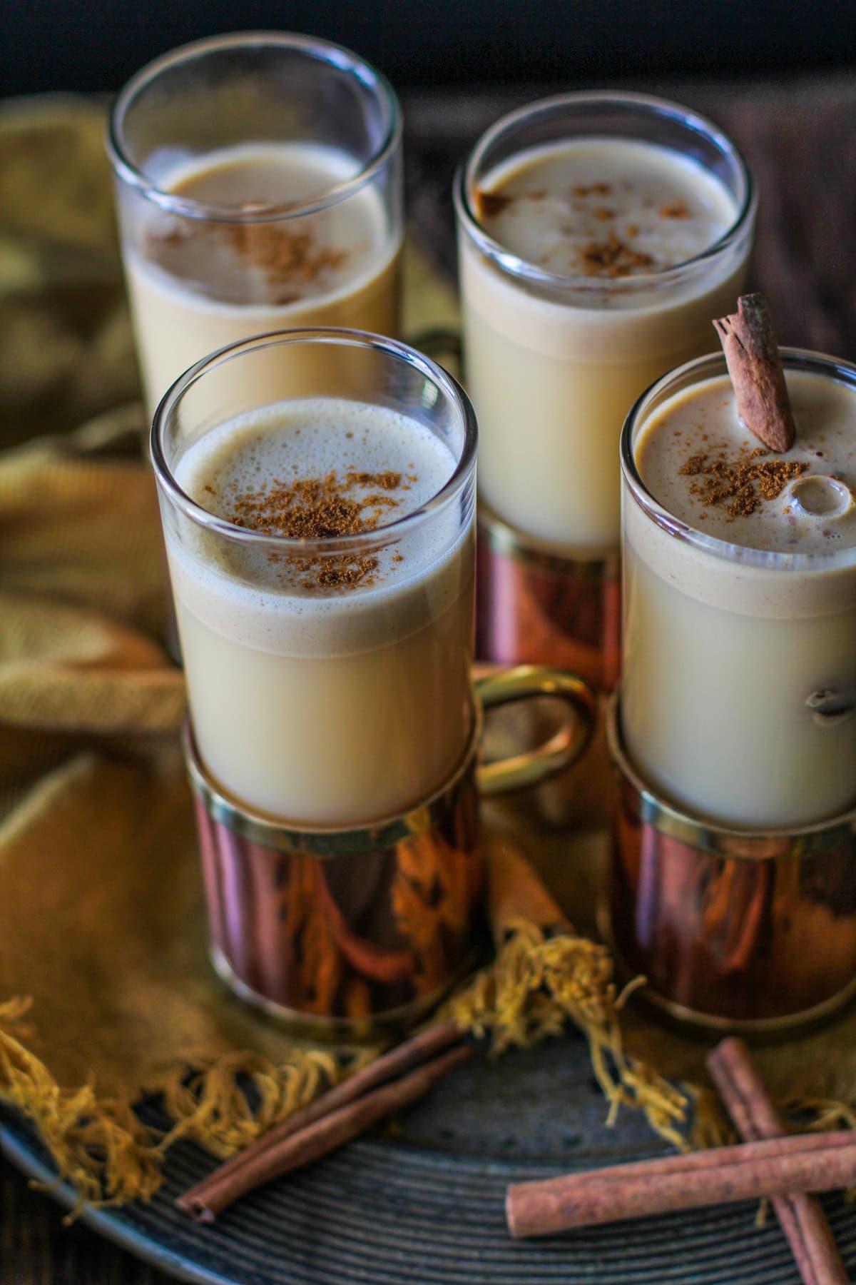 Four glasses of Hot Buttered Rum with Cider and cinnamon sticks sprinkled around.